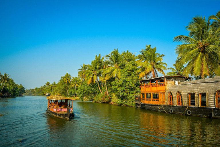 A tourist boat passes through a traditional Kerala houseboat on the backwater of Vembanad Lake